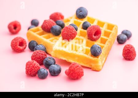 Waffles with blueberries and raspberries on pink background. Stock Photo