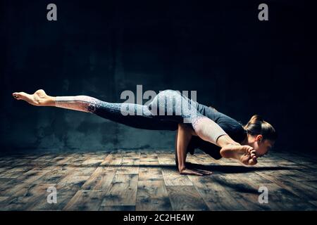 Young woman practicing yoga doing hurdler pose in dark room Stock Photo