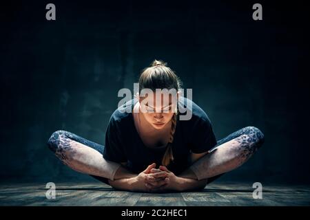Young woman practicing yoga doing reclined goddess pose asana in dark room Stock Photo