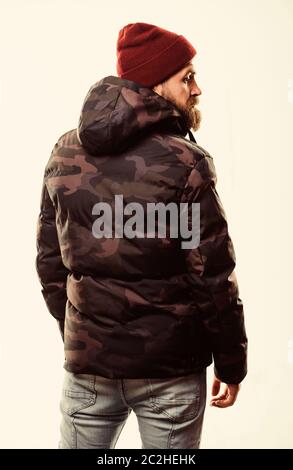 Hipster winter fashion. Guy wear hat and black winter jacket. Comfortable winter outfit. Winter stylish menswear. Man stand warm camouflage pattern jacket parka with hood isolated on white background. Stock Photo