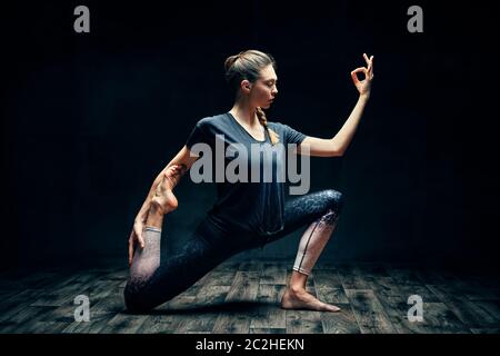 Young beautiful woman doing yoga asana one legged king pigeon pose in dark room Stock Photo