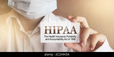 Doctor wearing face mask shows a card with the text HIPPA, The Health Insurance Portability and Accountability Act of 1996,. Medical concept. Stock Photo