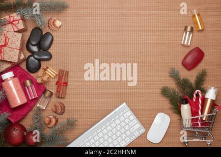 Shopping trolley, gift boxes, spa composition, computer keyboard and Christmas ornaments on bamboo mat background. Top view with copy space. Christmas Stock Photo