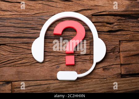 Customer Support Concept Headphones And Question Mark On Wooden Desk Stock Photo