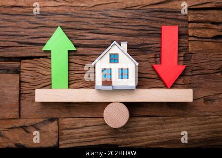 Up And Down Arrows And House On Seesaw On Wooden Desk Stock Photo