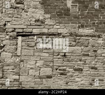 monochrome sepia toned image of a large old wall made of mixed bricks and stone with many patched and uneven repairs Stock Photo