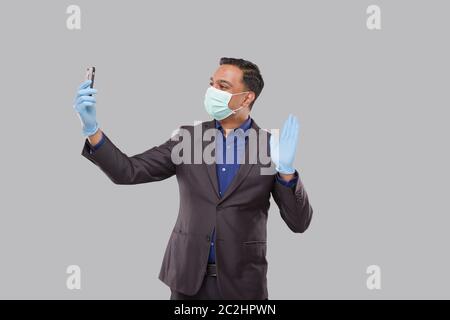 Businessman Having Video Call on Phone Wearing Medical Mask and Gloves Isolated. Indian Man Businessman Video Call. Business Online. Businessman Using Stock Photo