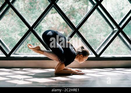 Young beautiful woman doing yoga asana baby crow pose on triangular window background Stock Photo