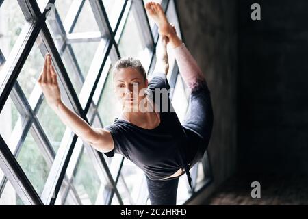 Young beautiful woman doing yoga asana natarajasana on large triangular window background Stock Photo