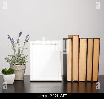 empty white photo frame, stack of books and a pot of growing lavender on a black table, workplace Stock Photo