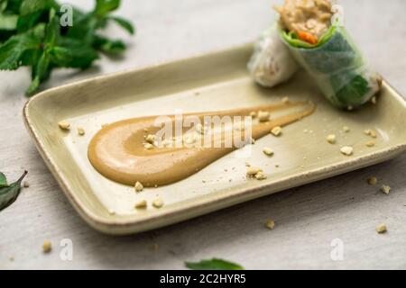 Delicious creamy peanut butter dipping sauce on a plate with crunchy peanut crumbs and Vietnamese spring rolls on the side. Peanut butter sauce is oft Stock Photo
