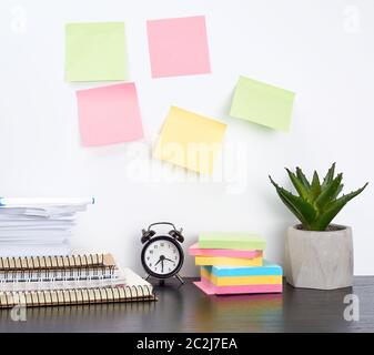 stack of spiral notebooks and colored stickers, next to a ceramic pot with a flower on a black table, white wall, Scandinavian-style minimalism Stock Photo