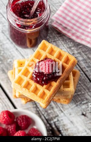 Tasty sweet waffles with raspberries and jam on white wooden table. Stock Photo