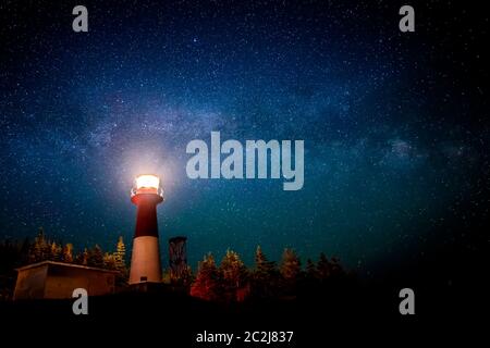 A lighthouse at night with a star filled sky above. The light in the top of the lighthouse is illuminated. The Milky Way is visible. Stock Photo