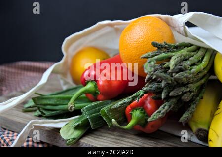 Cloth bag peppers, asparagus, oranges and bananas on a wooden table and dark background Stock Photo