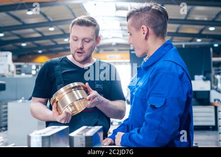 Skillful master discussing a workpiece with his apprentice or trainee Stock Photo