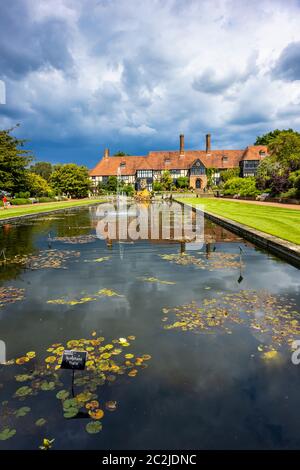 View of the iconic, historic Laboratory Building along the Jellicoe Canal under heavy grey skies at RHS Wisley Garden in Surrey, southeast England