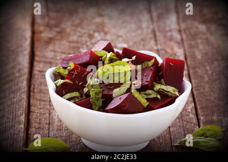 Beetroot chopped for salad with basil and dill seeds in bowl on rustic wooden table . Stock Photo