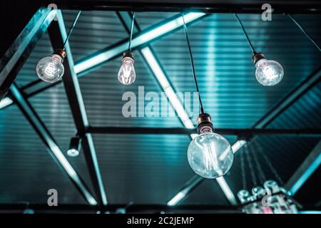 Group of teal and blue hanging lamps of different shapes and type of the spiral in a dark interior with crossing illuminating lines Stock Photo