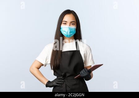 Covid-19, social distancing, small coffee shop business and preventing virus concept. Serious cute asian female barista, waitress taking client order Stock Photo