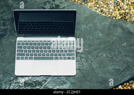 Laptop computer mockup has empty screen outside on stone in garden of coffee shop. Stock Photo