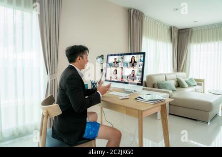 Mixed race businessman wearing Formalwear business suit on top and boxer pants on bottom, showing other people on screen in formal fridays business ou Stock Photo