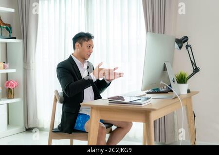 Mixed race businessman wearing Formalwear business suit on top and boxer pants on bottom, showing other people on screen in formal fridays business ou Stock Photo