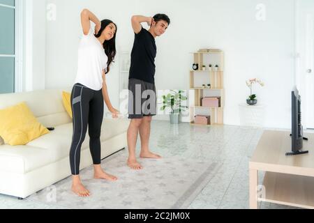 Young Asian couple doing High-intensity interval training together and looking TV at home, man and woman working out together standing in living room, Stock Photo