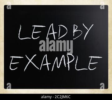 "Lead by example" handwritten with white chalk on a blackboard. Stock Photo