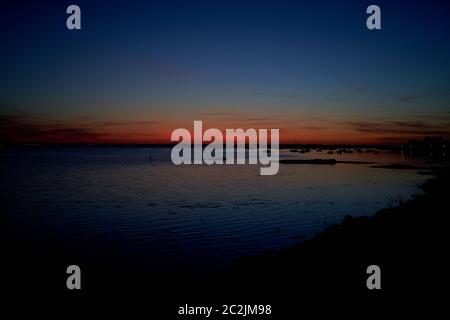 Arcachon bay at sunset, a fisherman stands in the water and a small fishing boat passes, Gironde, France Stock Photo
