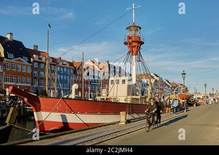 People cycling through colourful facades and restaurants on Nyhavn embankment and old ships along th Stock Photo