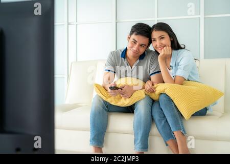 Asian happy fcouple sitting in sofa and watching television at home concept of family values, vacation day, holiday, happiness or lifestyle. Stock Photo