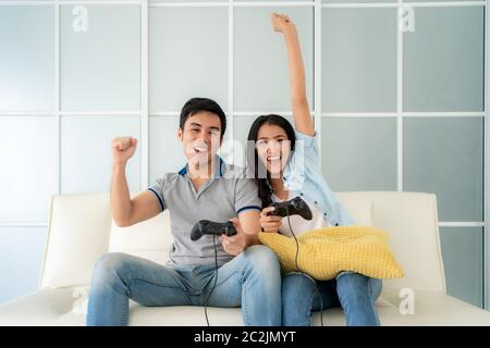 Happy Asian Couple Playing Computer Video Game Sitting On Couch At