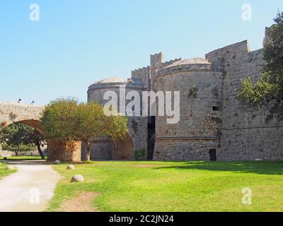 people crossing the amboise gate in the medieval walls of the old city in rhodes town surrounded by grass and trees Stock Photo