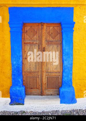 old ottoman style ornate wooden door double in a bright blue painted stone frame set in a yellow wall in rhodes town greece Stock Photo