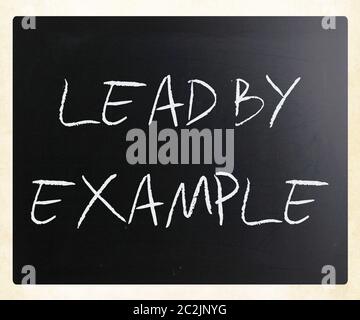 "Lead by example" handwritten with white chalk on a blackboard. Stock Photo
