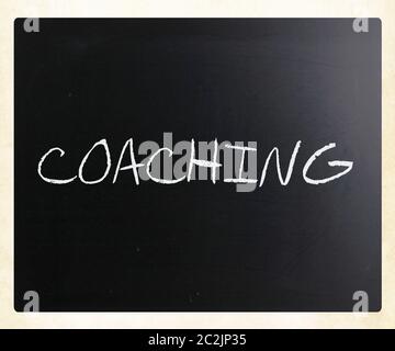 'Coaching' handwritten with white chalk on a blackboard. Stock Photo