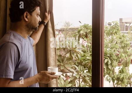 Man holding a tasty cup of sweet smelling morning coffee, relaxing and looking through the window. Morning sun light coming from outside. Happy weeken Stock Photo