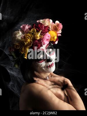 Young beautiful girl with traditional mexican death mask. Calavera Catrina. Sugar skull makeup. girl dressed in a wreath of roses on a background of w Stock Photo