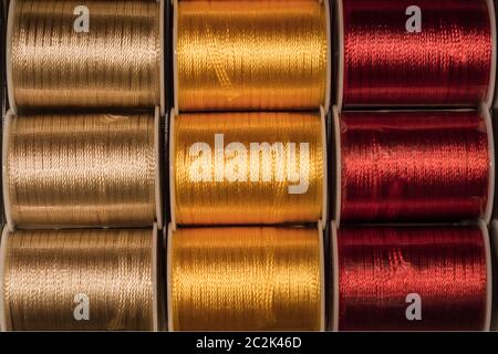 Cutout texture closeup on coils of colored sewing threads gold, yellow and red. Stock Photo