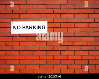 a white sign saying no parking on a red brick wall Stock Photo