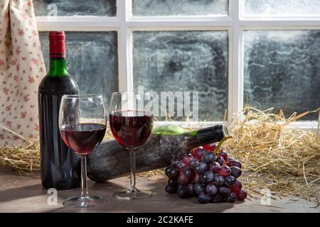 Composition with two wineglasses, grapes and bottles of red wine, window at background Stock Photo