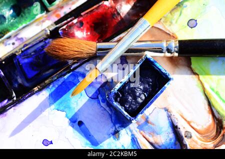 Two crossed watercolor brushes over a watercolor paint box Stock Photo