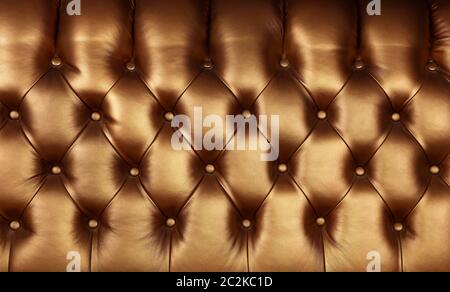 Background texture of dark golden brown capitone genuine leather, retro Chesterfield style soft tufted furniture upholstery with deep diamond pattern Stock Photo