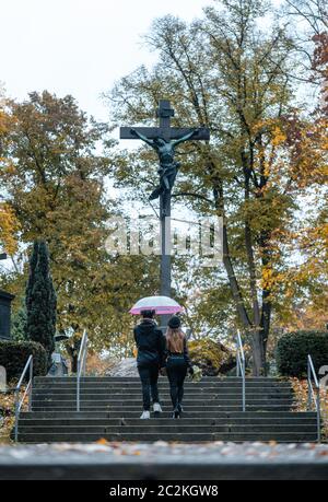 Man and woman walking up steps on cemetery towards a cross in autumn Stock Photo