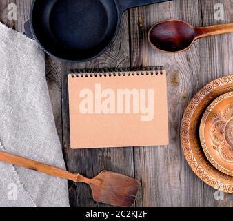 empty black round frying pan with handle, spoon and paper notebook on a wooden table, top view Stock Photo