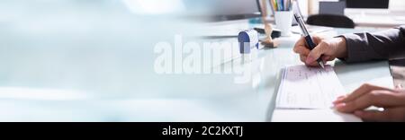 Close-up Of A Businessman Filling The Cheque With Pen On Reflective Desk In Office Stock Photo