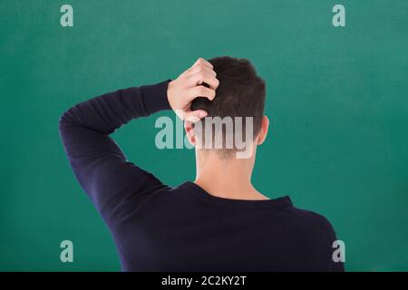 Rear View Of Young Man In Blue T-shirt Scratching His Head Against Green Background Stock Photo