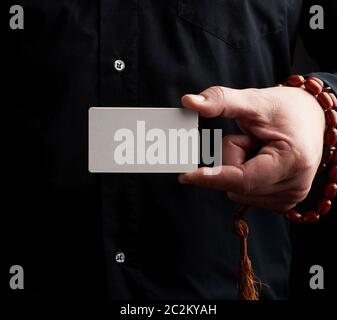 male hand holding a rectangular blank white paper business card, man wearing a black shirt, place for inscription Stock Photo