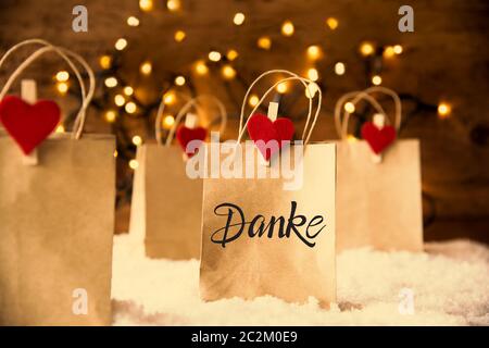 Christmas Shopping Bags On Snow With German Calligraphy Danke Means Thank You. Bright Glowing Lights In Background Stock Photo